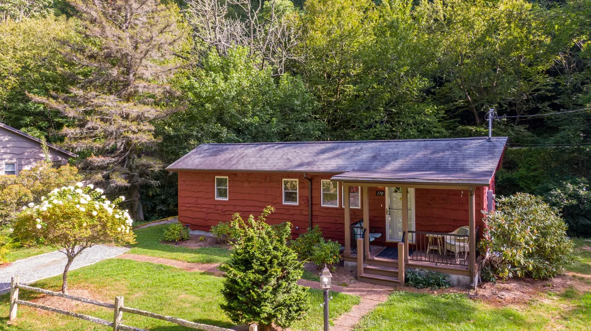 This exterior shot highlights the vibrant red exterior of the house, its cozy porch, and the surrounding greenery. The inviting porch suggests relaxation and the potential for enjoying the natural environment, while the lush backdrop hints at proximity to trails and picturesque drives.