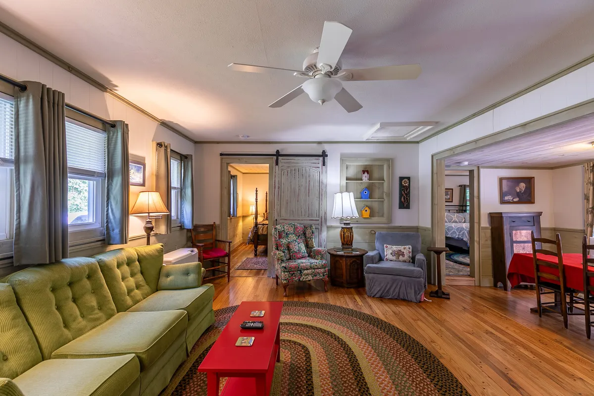 The living room is pictured from a different angle, highlighting the green sofa, red coffee table, floral armchair, and warm lighting from the lamps. The setup invites relaxation and intimate gatherings, while the room's decor enhances its cozy, welcoming vibe.