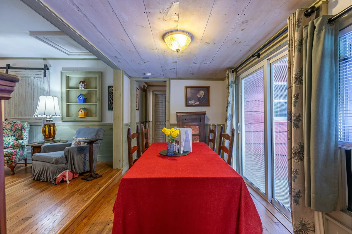 A bright, inviting dining area features a red dining table, yellow flowers at the centerpiece, a comfortable armchair, and a bright lamp, all set in a space perfect for family gatherings or sharing meals after a day of adventure.